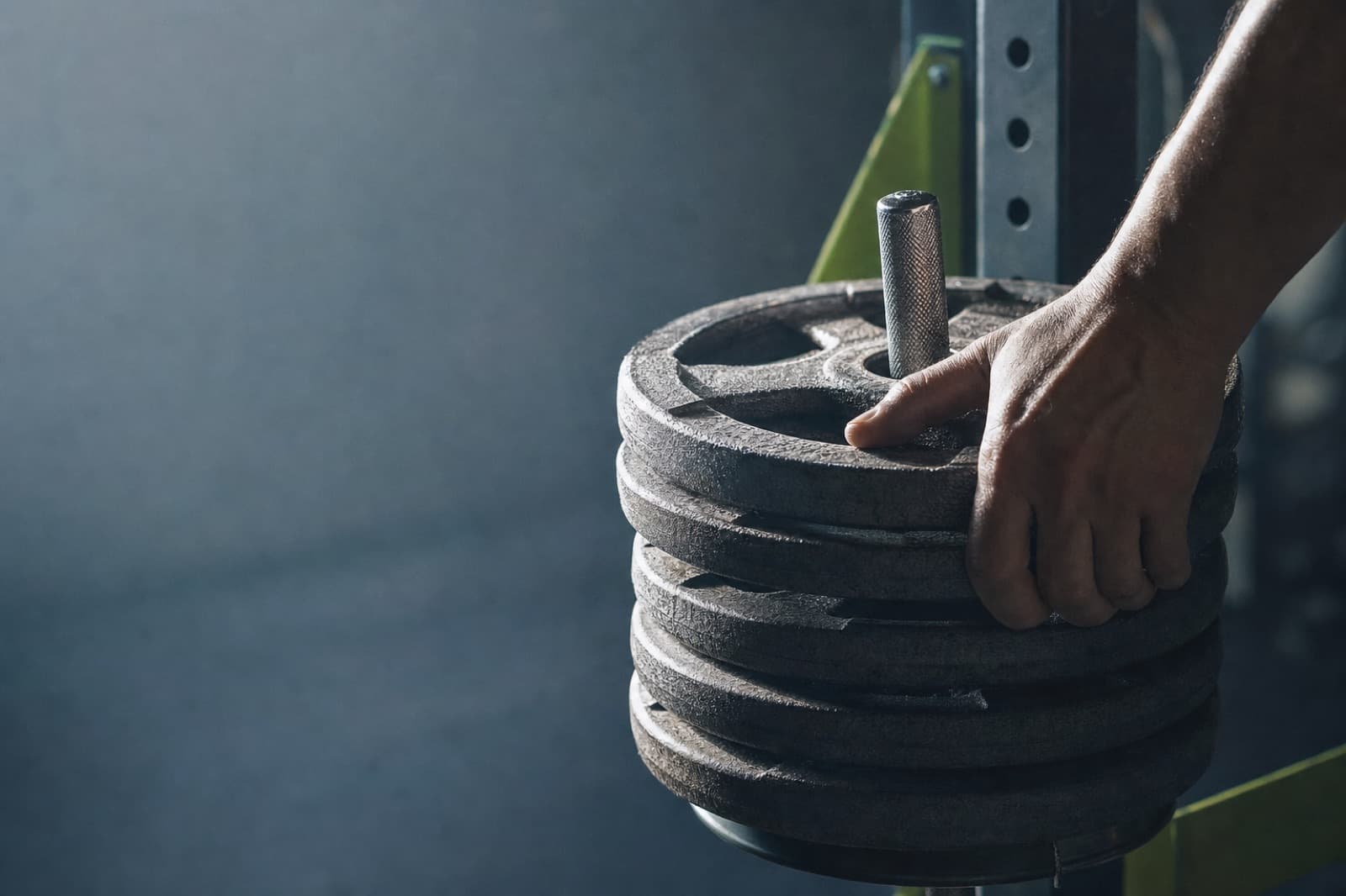 A hand reaching for the top of a stack of weight plates on a rack